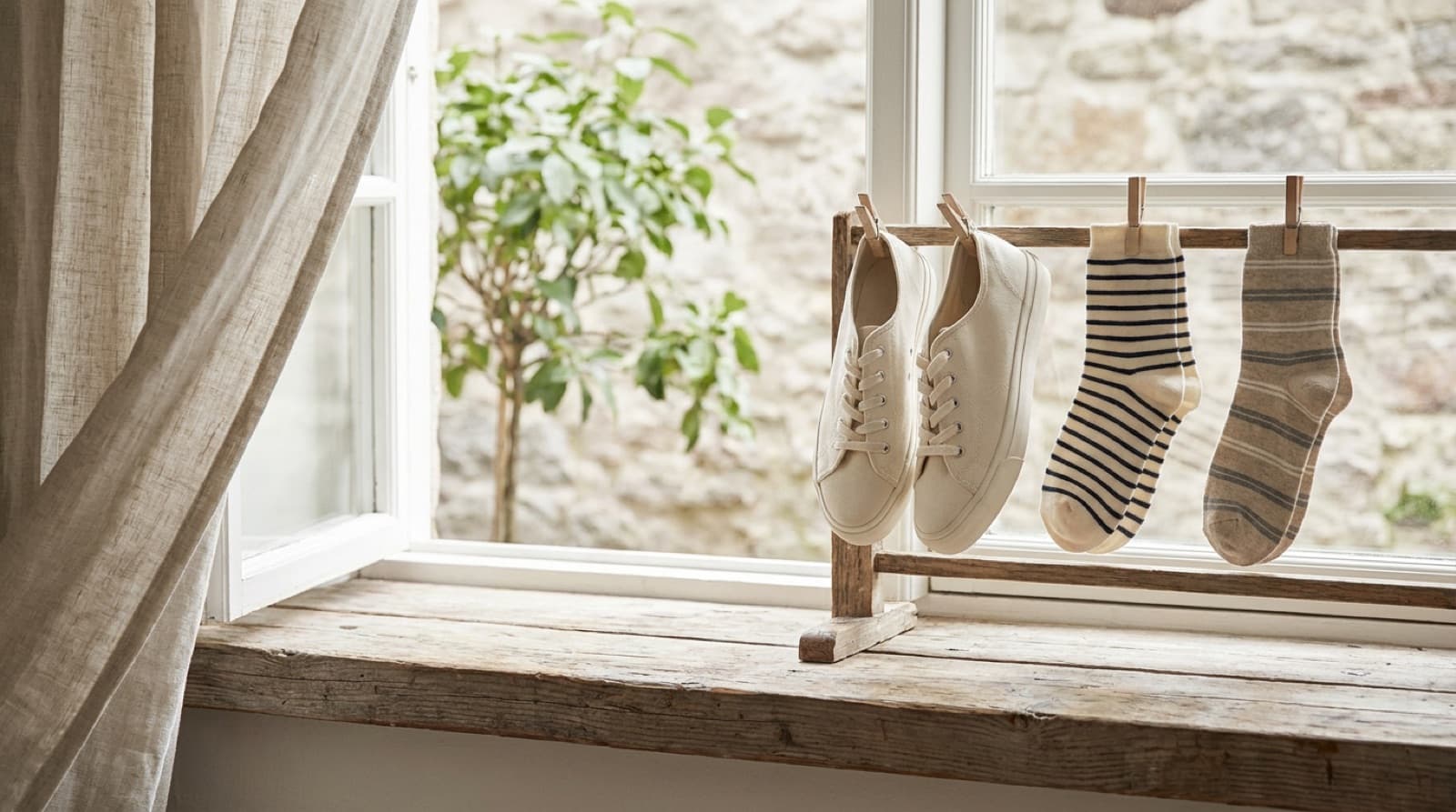 Helle Stoffturnschuhe und zwei Paar frisch gewaschene Socken trocknen an einem offenen Fenster